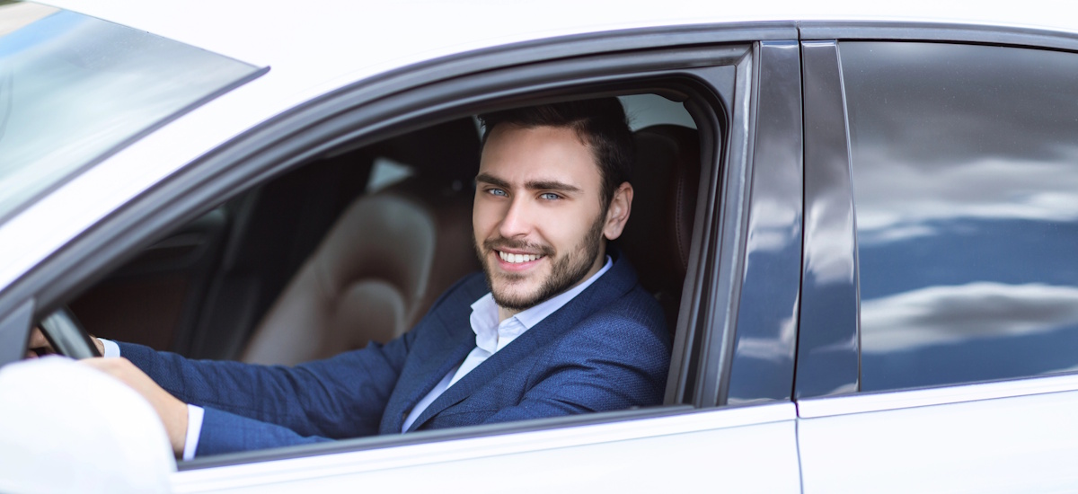 Geschäftsmann sitzt am Steuer eines Autos und lächelt aus dem Fahrerfenster – Beispiel für Fahrzeugnutzung im Modell Leasing statt Kauf