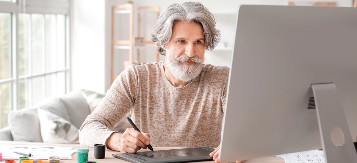 Rentner arbeitet am Computer mit Grafiktablett im Homeoffice – Beispiel für selbstständig Rentner im Ruhestand