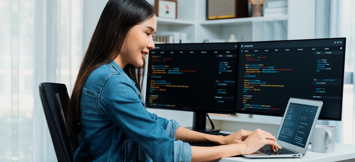 IT-Selbstständige arbeitet am Laptop mit zwei Monitoren und Programmiercode – Beispiel für selbstständig in der IT im Homeoffice
