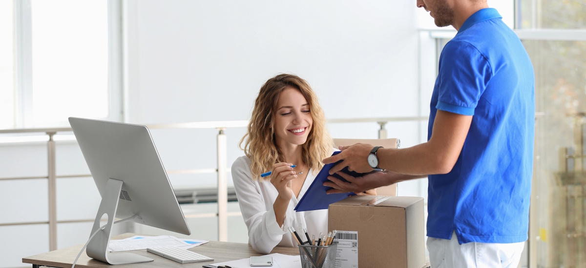 Lieferschein: Empfängerin bestätigt eine Paketzustellung auf dem Klemmbrett eines Zustellers im Büro.